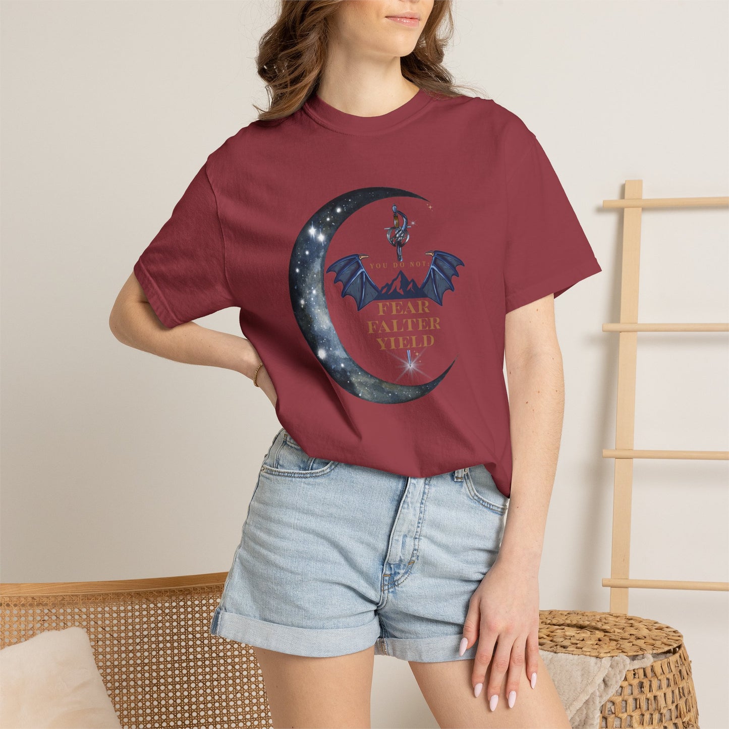 Person wearing a maroon t-shirt with a graphic design and denim shorts in a casual setting.